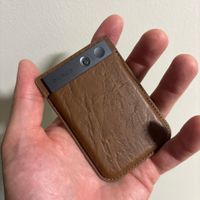 A small brown leather wallet or card holder being held in an open palm, with a gray card or device visible inside it